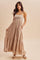 woman wearing a tan maxi dress with spaghetti straps, smocked bodice, and tiered skirt, standing with hands in pockets