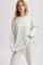 woman wearing a cream and light blue striped long sleeve top with relaxed fit and holding the hem, paired with gray pants
