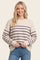 woman wearing a cream and purple striped knit sweater, smiling and holding her waist with blue jeans