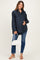 woman wearing a navy polka dot maternity button-up shirt and blue jeans, cradling her baby bump and holding a white handbag