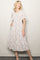 woman wearing a white floral midi dress with puff sleeves and gathered detailing, standing with a smile