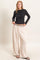 woman wearing a black long sleeve top with asymmetrical design and light beige wide-leg pants with drawstring waist