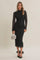 woman wearing a black lace long sleeve midi dress, holding a silver handbag and wearing black heels