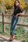 woman wearing a black sheer sleeve top and high-waisted blue jeans, standing by a wooden fence outdoors