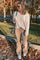 woman wearing a cream oversized knit sweater and tan flared corduroy pants, holding a drink and standing outdoors