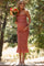 woman wearing a rust-colored maternity dress with ruffle details and holding a bouquet of flowers while showing her baby bump