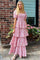 woman wearing a pink floral tiered maxi dress with puff sleeves standing in front of a brick wall