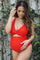 woman wearing a red maternity swimsuit with a cutout design and holding her baby bump