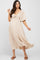 woman wearing a beige short sleeve maternity dress with a tie front detail and flowing skirt, showcasing her baby bump