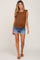 woman wearing a brown ribbed maternity top with ruffle sleeves and denim shorts, showing her baby bump