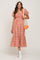 woman wearing a red and white gingham maternity dress with puff sleeves and a tiered skirt, holding a net bag with oranges