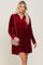 woman wearing a long sleeve burgundy velvet button down mini dress with a tan quilted crossbody bag
