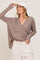 woman wearing a taupe textured button-up sweater with long sleeves and a relaxed fit, paired with light-colored pants and a cap