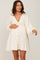 woman wearing a creamy white maternity dress with lace detail and button front, gently holding her baby bump