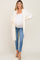 woman wearing a cozy white maternity cardigan over a fitted tank top and blue jeans, showing her baby bump