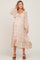 woman wearing a cream floral maternity dress with long sleeves and a ruffled hem, showcasing her baby bump