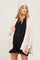 woman wearing a light pink knitted maternity cardigan and a matching beanie over a black button-up maternity romper