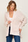 woman wearing a light pink open knit cardigan with a pocket, styled over a white top and blue jeans