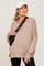 woman wearing a beige oversized maternity sweater with dropped shoulders and side slits, accessorized with a black crossbody bag and cap