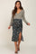 woman wearing a gray long sleeve maternity wrap dress with a floral patterned skirt and a side slit, showing her baby bump