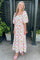 woman wearing a floral print maxi dress with puff sleeves and a square neckline, standing outdoors with plants in the background