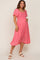 woman wearing a pink maternity dress with puff sleeves and a smocked bodice, showcasing her baby bump.