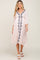 woman wearing a light pink maternity dress with navy floral embroidery and a tie waist detail