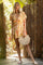 woman wearing a floral mini dress with a tie front and holding a woven handbag, standing in a tropical setting