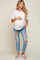 woman wearing a white short sleeve maternity top and distressed blue maternity jeans, holding her baby bump