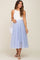 woman wearing a white sleeveless top and a light blue maternity tulle skirt, holding her baby bump with a handbag