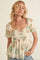woman wearing a cream floral puff sleeve top with a sweetheart neckline and gold pearl necklaces