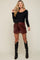 woman wearing a black long sleeve maternity top and burgundy faux leather shorts, paired with black knee-high boots