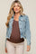 woman wearing a light wash denim maternity jacket with ruffle hem and long sleeves, holding her baby bump