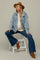 woman wearing a distressed denim jacket over a beige maternity top and blue flared jeans, sitting on a stool with a baby bump visible