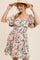woman wearing a floral puff sleeve mini dress with a smocked waist and square neckline, smiling with a straw hat