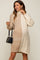 woman wearing a beige and cream color block cable knit maternity sweater dress with turtleneck and holding a small handbag