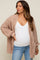 Pregnant woman wearing a mauve chunky knit cardigan over a white maternity tank top and blue jeans