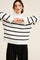 woman wearing a white and black striped oversized sweater with wide sleeves and high neckline