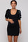 woman wearing a black ribbed maternity dress with sequin puff sleeves and showing her baby bump