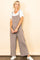 woman wearing a taupe jumpsuit over a white t-shirt, standing with hands relaxed and smiling