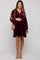 woman wearing a burgundy velvet maternity dress with floral sleeves and holding her baby bump