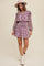 woman wearing a purple floral mini dress with ruffle details and long sleeves, paired with a pink hat and white ankle boots