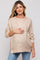 woman wearing a beige maternity sweater with speckled details and holding her baby bump