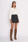 woman wearing a white long sleeve henley top and a black button-front mini skirt with brown knee-high boots