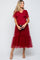 woman wearing a burgundy maternity dress with short tulle sleeves and a tiered tulle skirt, holding a clutch and showcasing a baby bump