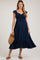 woman wearing a navy blue maternity dress with ruched detailing and flutter sleeves, holding a woven bag