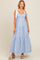 woman wearing a light blue tiered maxi dress with adjustable white tie straps and smocked bodice, standing on a neutral background
