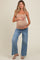 woman wearing a nude maternity tank top and blue wide-leg jeans, holding her baby bump