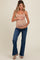 woman wearing a beige maternity tank top and holding her baby bump, paired with flared blue jeans and heeled sandals