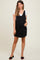 woman wearing a black maternity overall dress with pockets over a white top and styled with black slide-on shoes
